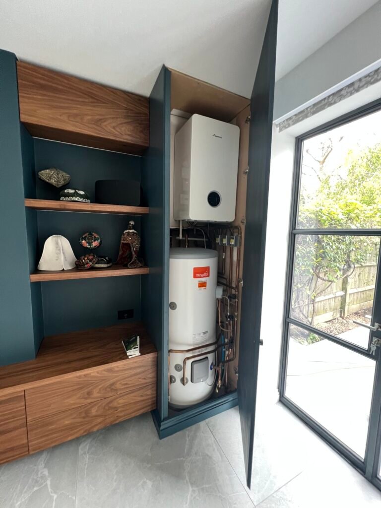 Built-in boiler and hot water cylinder cupboard with bespoke joinery and walnut shelving, designed and installed by Torwood Interiors in Richmond