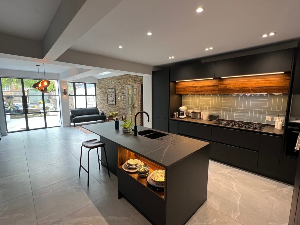 Open-plan kitchen extension in St Margarets featuring black cabinetry, walnut accents, and slim steel doors — designed and built by Torwood Interiors.