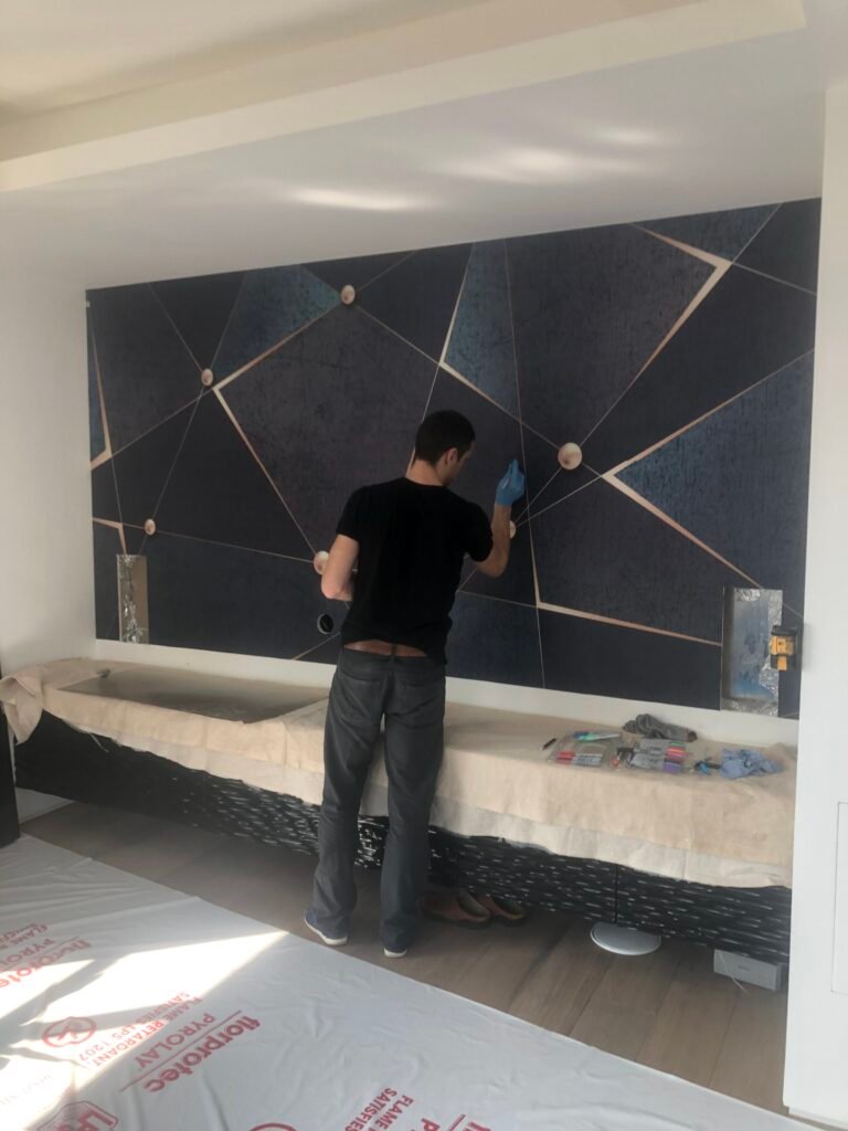 Work in progres. A modern living room in Purley, featuring a deep blue feature wall, bespoke TV joinery, and geometric wallpaper with ambient lighting. Designed and built by Torwood Interiors to blend character, comfort, and contemporary style